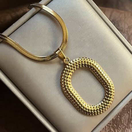 Gold necklace with a textured pendant on a light gray surface