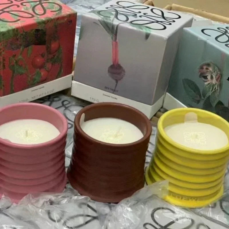 Stacked candles in pink, brown, and yellow pots with boxes in the background.