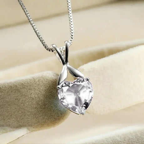 Heart-shaped crystal pendant on a chain against a beige background
