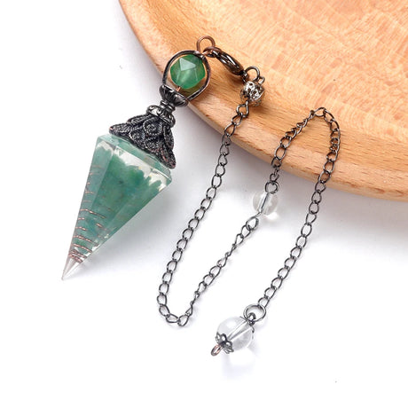 Crystal pendulum with green stone on a wooden surface