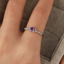 Silver ring with a purple gemstone on a person's finger against a neutral background