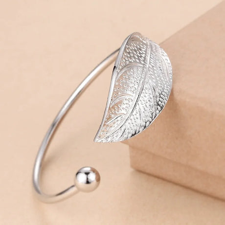 Silver leaf-shaped bracelet on a beige background
