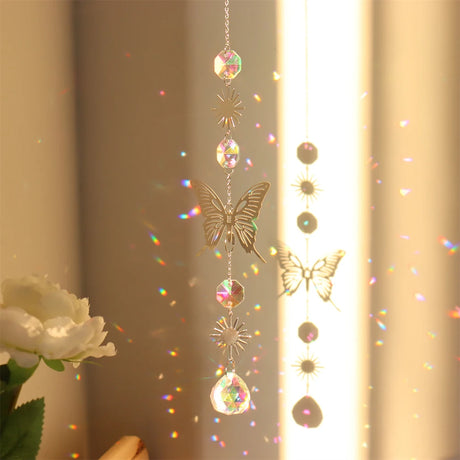 Butterfly-shaped crystal hanging ornament with rainbow, next to a white rose.
