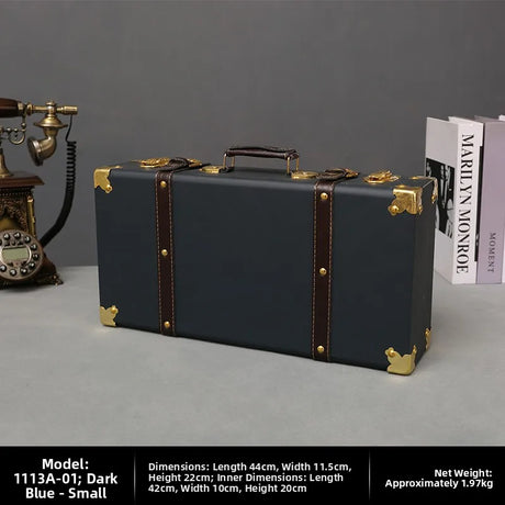 Dark blue suitcase with gold accents on a gray surface with books and a vintage phone in the background.