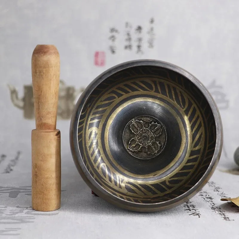 Bronze singing bowl with wooden handle on a textured surface
