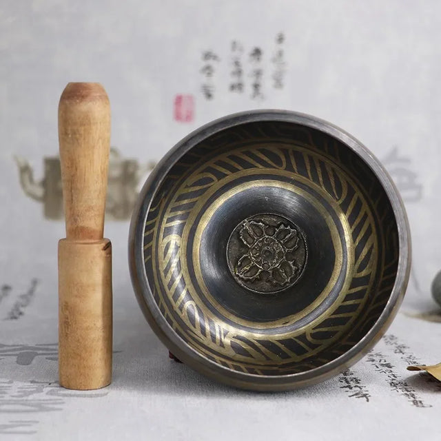 Bronze singing bowl with wooden handle on a textured surface