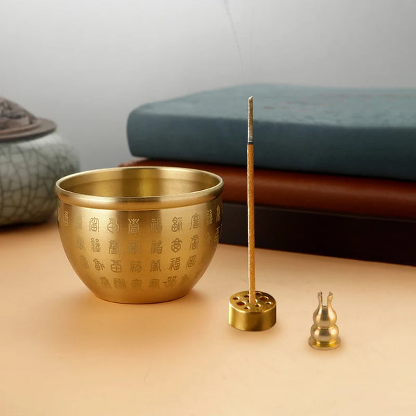 Brass incense bowl with incense stick holder and two incense sticks on a beige surface.