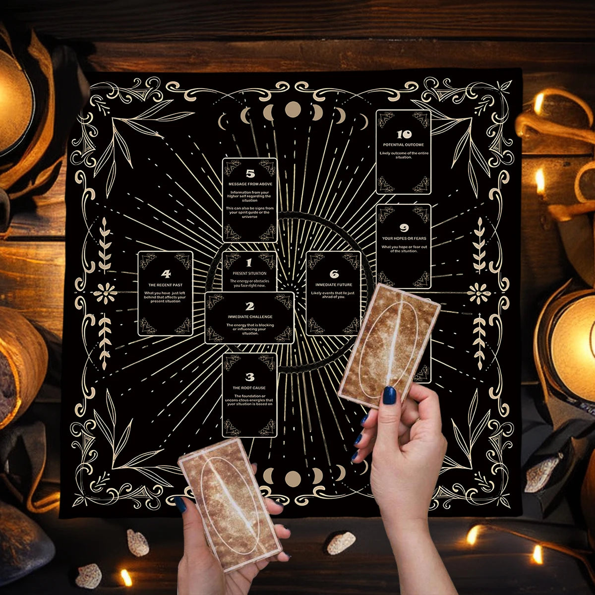 Person holding tarot cards in front of a decorative black and white tarot card layout with candles and stones on a wooden surface.