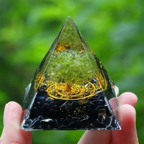Pyramid-shaped crystal with gold interior held by a hand against a green blurred background