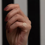 Gold necklace with a tree pendant held by a hand against a dark background