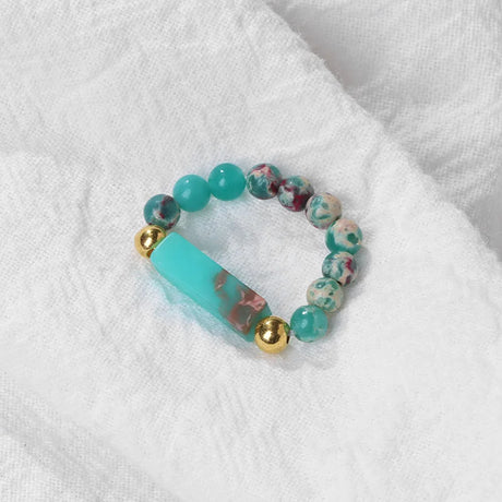 Turquoise beaded bracelet with gold accents on a white fabric background