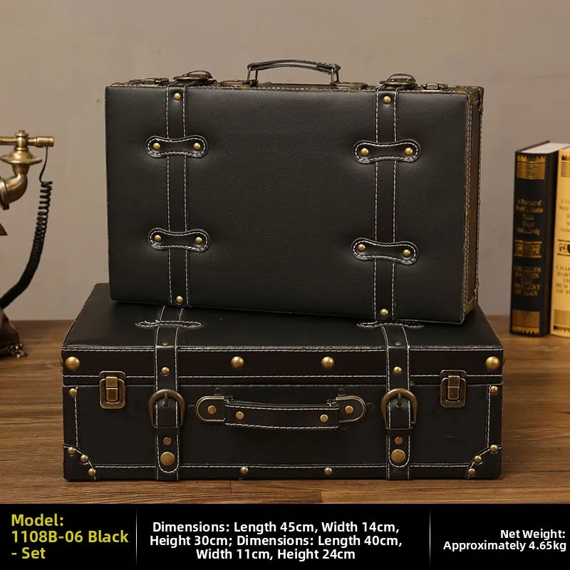Two black leather suitcases stacked on a wooden surface with a vintage phone and books in the background.