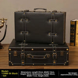 Two black leather suitcases stacked on a wooden surface with a vintage phone and books in the background.