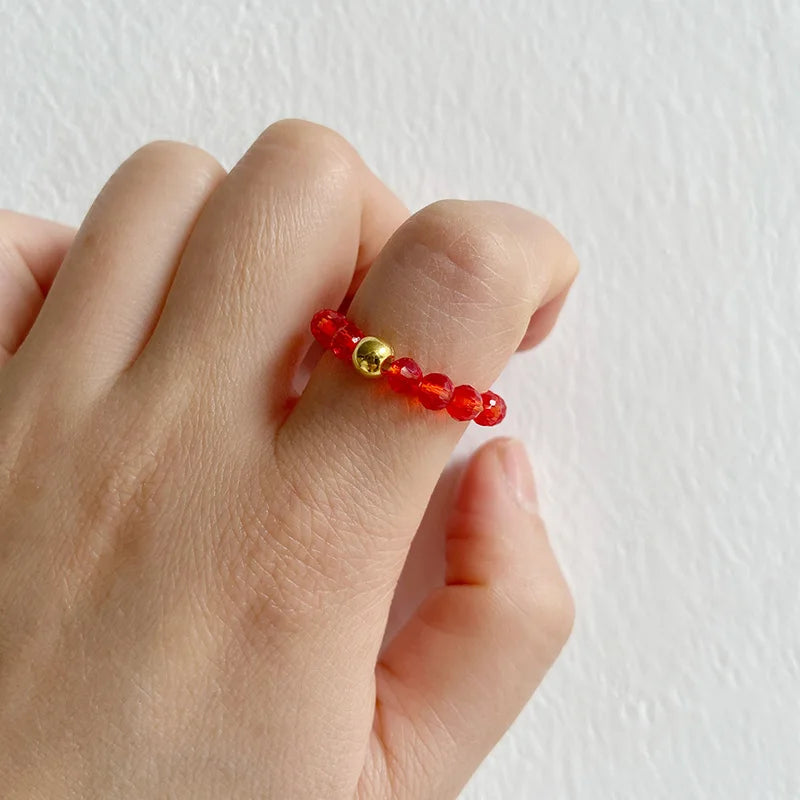 Hand wearing a red beaded ring with a gold accent on a light background