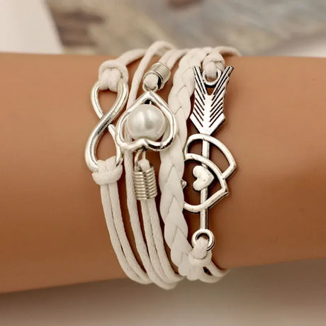 White leather bracelet with silver charms on a wrist against a neutral background