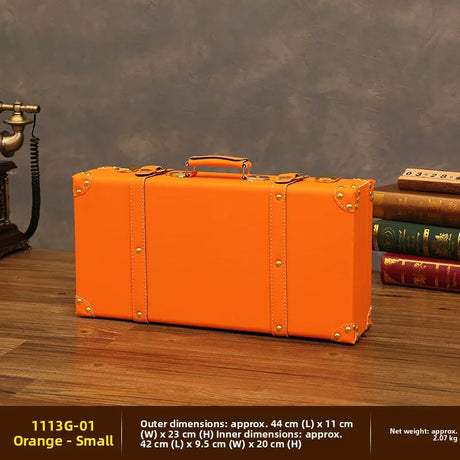 Orange suitcase on a wooden surface with books and a vintage phone in the background