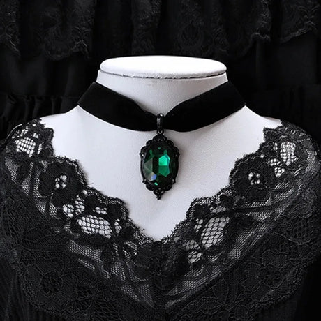 Black lace garment with a green gemstone necklace on a mannequin against a black background