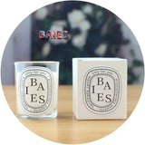 Candle and packaging with 'BAIES' branding on a blurred floral background