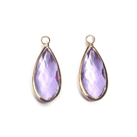 Two teardrop-shaped purple gemstones with gold settings on a white background