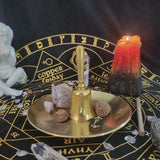 Witchcraft altar setup with a gold bell, crystals, and a candle on a black and gold astrological circle.