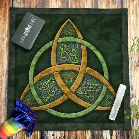 Triquetra symbol on a green cloth with tarot cards and a crystal on a wooden surface