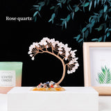 Decorative crystal tree with rose quartz on a white surface, candle, and framed picture in the background.