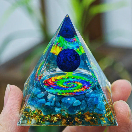 Triangular pyramid with colorful spiral design and blue stones held by a hand against a blurred green background