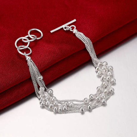 Silver bracelet with multiple chains and beads on a red fabric background