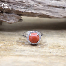 Ring with a coral stone and diamond halo on a wooden surface