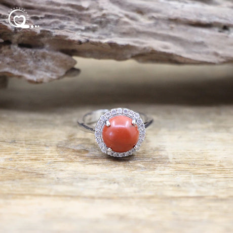 Ring with a coral stone and diamond halo on a wooden surface