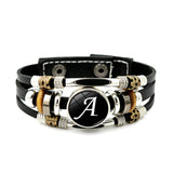 Multistrand leather bracelet with metal accents and a central black roundel with letter 'A'.