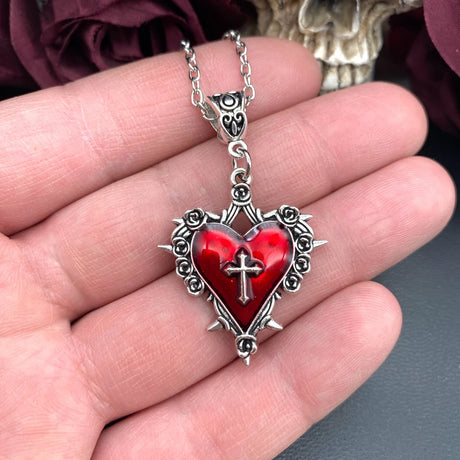 Heart-shaped pendant with red center and silver cross held in a hand