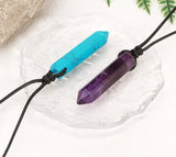 Two crystal necklaces, one blue and one purple, on a white rock with fern leaves in the background.