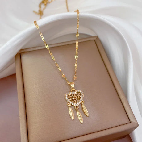 Gold necklace with a heart-shaped pendant and feather details on a beige box.
