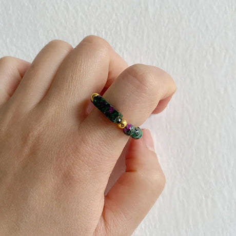 Hand wearing a ring with green gemstones on a plain background