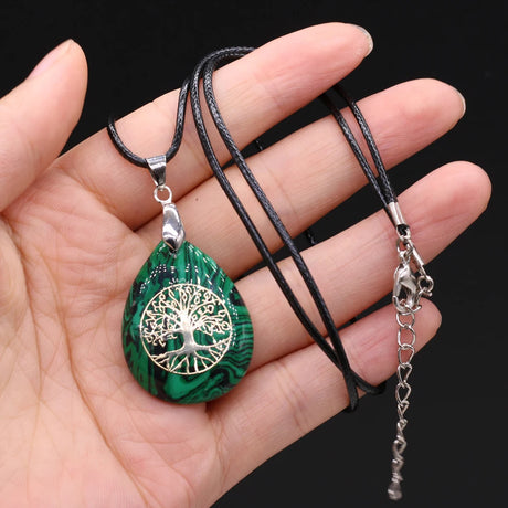 Green marbled pendant with silver tree design on a black cord held in hand against a black background