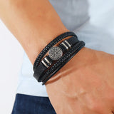 Black braided leather bracelet with a silver emblem on a wrist against a neutral background