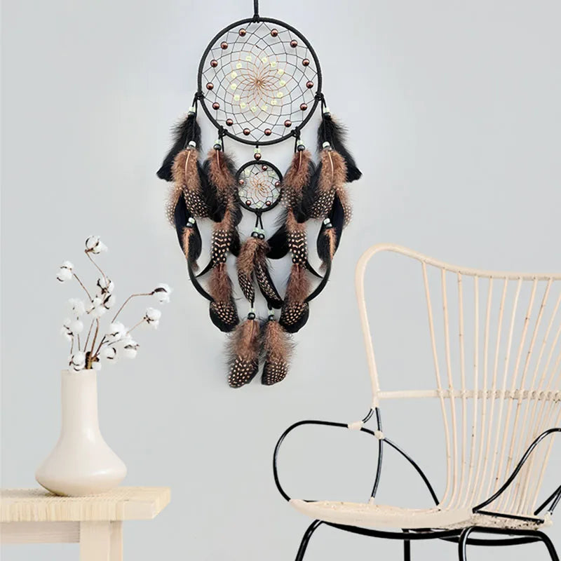 Decorative dreamcatcher with feathers hanging on a light gray wall next to a wicker chair and small table.