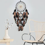 Decorative dreamcatcher with feathers hanging on a light gray wall next to a wicker chair and small table.
