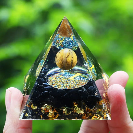 Pyramid-shaped crystal with intricate designs held by a hand against a green blurred background