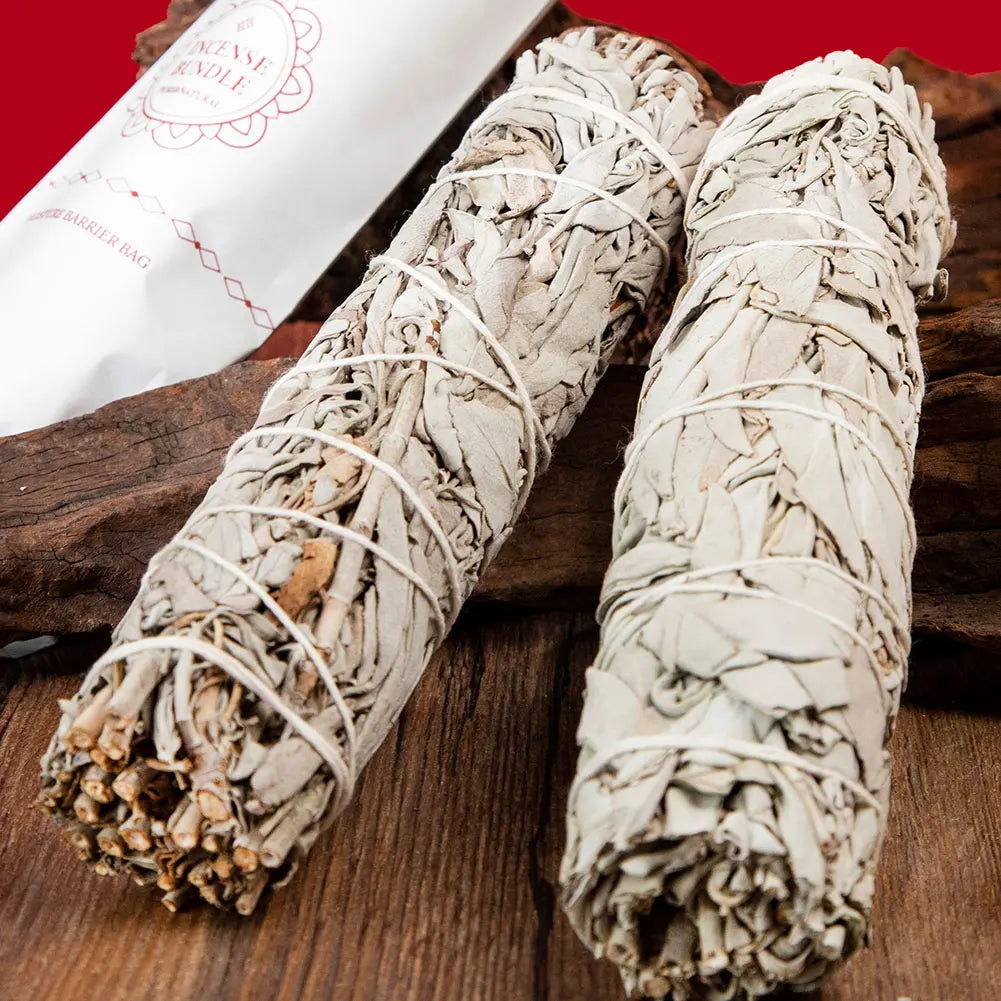 Two white sage smudge sticks on a wooden surface with a red background