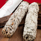 Two white sage smudge sticks on a wooden surface with a red background