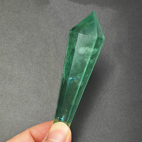 Green crystal held by a hand against a gray background