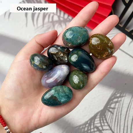 Hand holding a collection of ocean jasper stones with a red object in the background.
