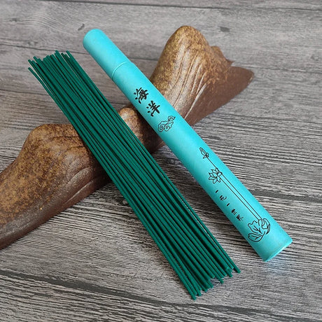 Turquoise incense stick holder with green incense sticks on a wooden surface