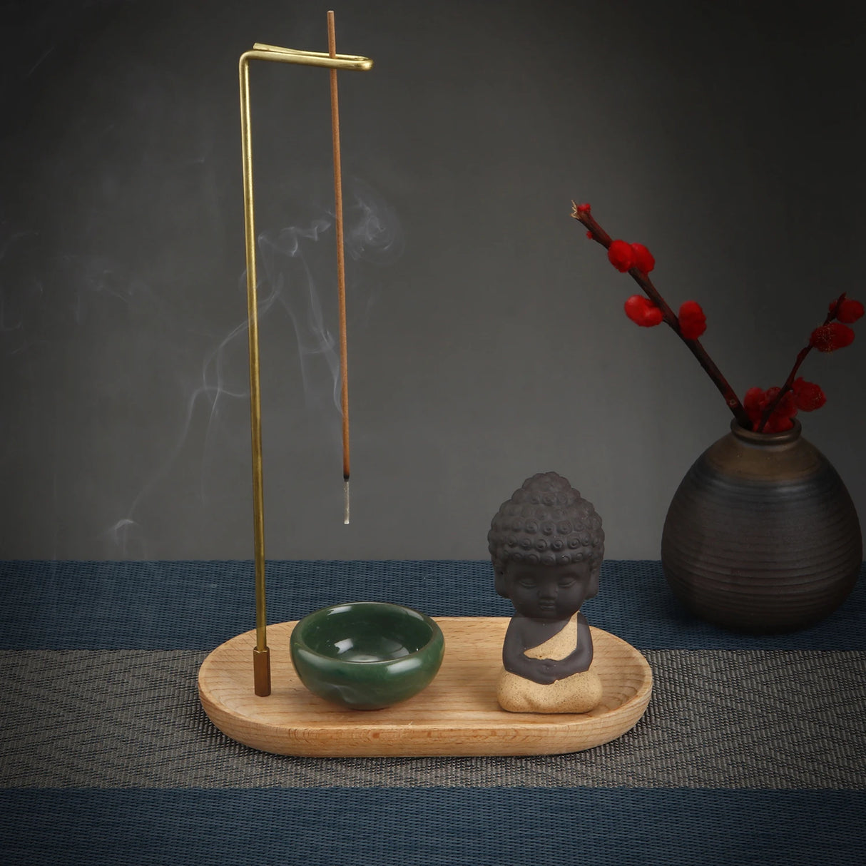 Incense burner with incense sticks, a small Buddha statue, and a vase with red flowers on a dark surface.