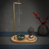 Incense burner with incense sticks, a small Buddha statue, and a vase with red flowers on a dark surface.