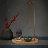 Decorative setup with a vase, Buddha statue, green bowl, and incense stick on a dark background