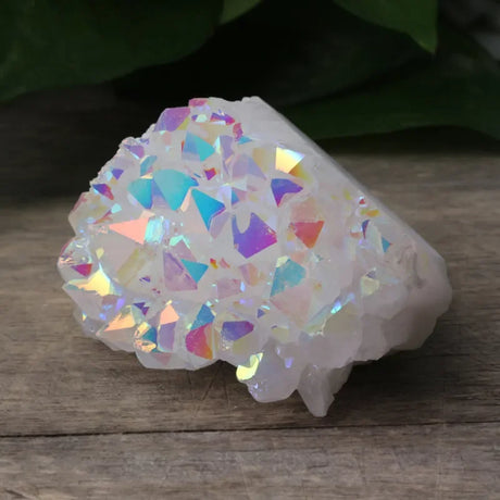 Iridescent crystal-like object on a wooden surface with greenery in the background