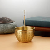 Gold incense burner with incense stick on a wooden surface